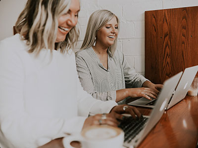 Two smiling women using laptops